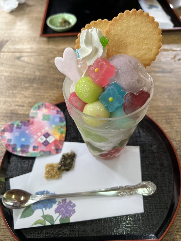 A colorful hydrangea-themed parfait loaded with mochi balls, flower-shaped jellies, purple ice cream, and a wafer cookie — served at a seasonal tea house inside Mimuroto-ji temple grounds.
